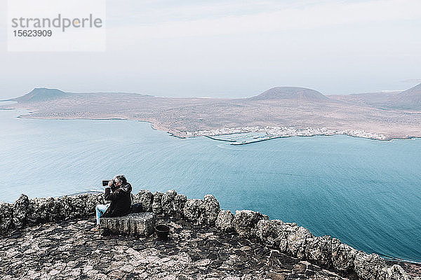 Mann schaut durch ein Fernglas auf die Landschaft mit der Isla de La Graciosa von einem Aussichtspunkt am Mirador del Rio  Lanzarote  Kanarische Inseln  Spanien