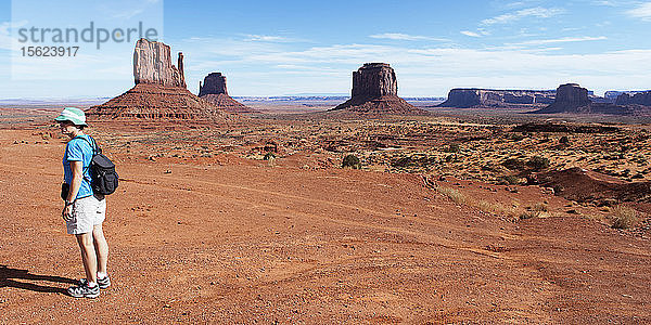 Eine Wanderin steht allein im Monument Valley und den Sandsteinfelsen.