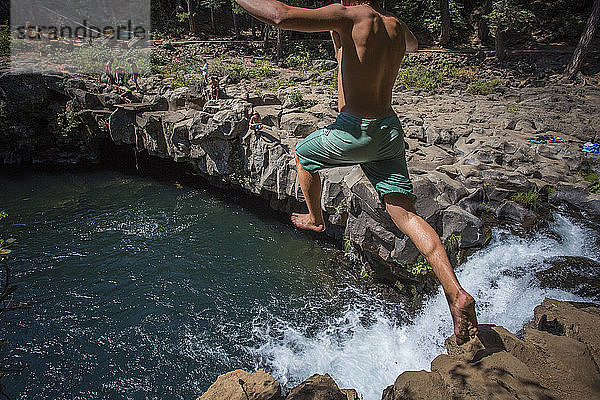 Rückansicht eines einzelnen hemdlosen jungen Mannes  der von der Klippe in den McCloudï¾ River springt  Kalifornien  USA