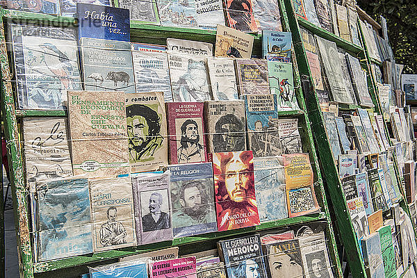 Ein Bücherregal am Straßenrand mit bunten kubanischen Geschichts- und Propagandabüchern  die auf dem berüchtigten Antiquitätenmarkt auf der Plaza de Armas  dem ältesten Platz der Stadt Havanna  zum Verkauf angeboten werden. Alt-Havanna (Havanna Veija)  La Habana  Kuba