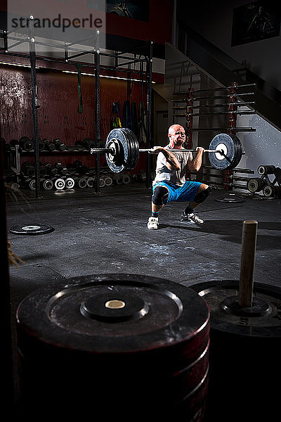 Ein athletischer Mann trainiert mit schweren Gewichten an einer Langhantel in einem düsteren Fitnessstudio in San Diego  Kalifornien.