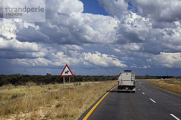 Auto auf der Straße in der Savanne und Schild  das vor wilden Tieren warnt  Namibia  Afrika