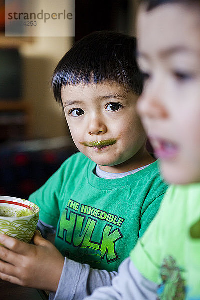 Ein 4 Jahre alter japanisch-amerikanischer Junge trinkt seinen morgendlichen grünen Smoothie neben seinem 6-jährigen Bruder.