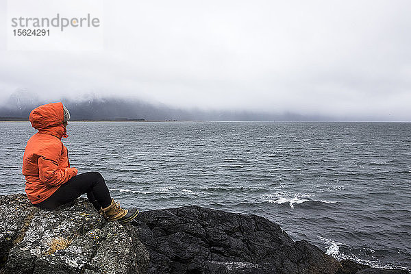 Der Profi-Snowboarder Robin Van Gyn sitzt an einem stürmischen Tag auf einem Felsen und blickt über den Ozean  während er einen Snowboardtrip nach Haines  Alaska  unternimmt.