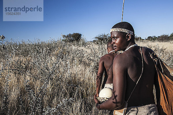 Foto von zwei Mitgliedern des San-Volkes  die durch das Unterholz in der Kalahari-Wüste  Botswana  wandern