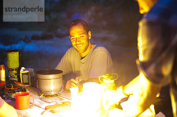 Ein Camper starrt lächelnd auf das Feuer eines Campingkochers.