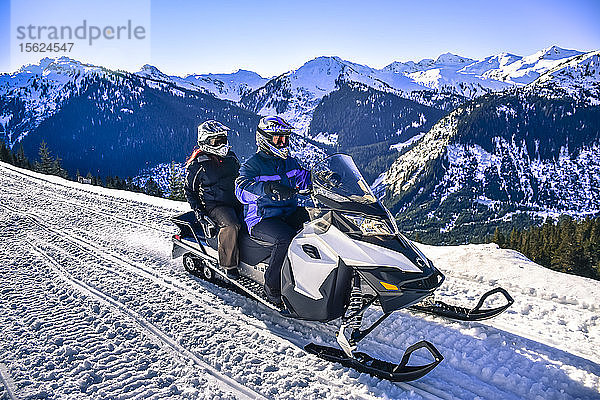 Mann und Frau fahren Schneemobil mit Berg im Hintergrund in Callaghan Valley  Whistler  British Columbia  Kanada
