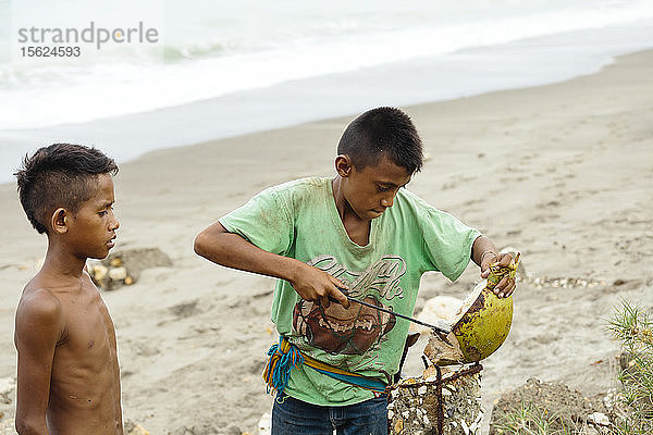 Jungen öffnen Kokosnuss am Strand  Sumba  Indonesien