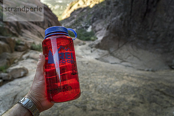 Ein Wanderer hält eine rote Wasserflasche