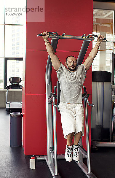 Porträt eines muskulösen Mannes  der an einem speziellen Sportgerät im Fitnessstudio trainiert