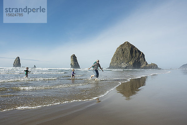 Mutter  Sohn und Tochter rennen vor den Wellen aus dem Ozean vor dem Haystack Rock am Cannon Beach  Oregon.