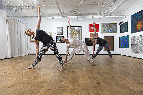 Drei Frauen in Dreieckspose Yoga Asana in einer Kunstgalerie