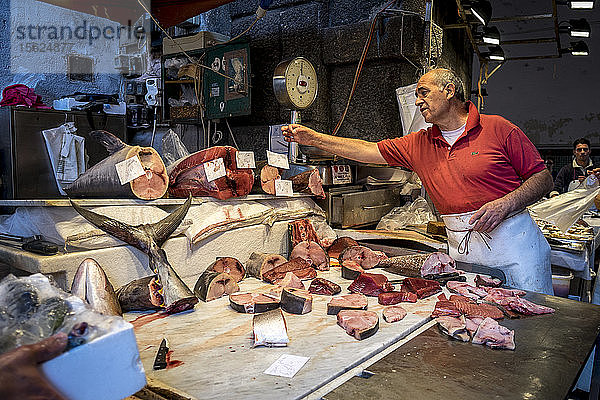 Ein Fischhändler beim Abwiegen von Fisch für einen Kunden in Sizilien  Catania
