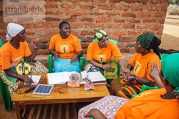 Mforo  Tansania ein Dorf in der Nähe von Moshi  Tansania. Die Solar Sisters treffen sich im Haus von Fatma Mziray??????  um ihre Geschäfte zu besprechen und Ideen auszutauschen. Sie genießen das Zusammensein und haben das Gefühl  dass es ihnen hilft  voneinander zu lernen und neue Verkaufs- und Marketingmethoden auszuprobieren. Durch die Gruppe sind sie alle enge Freundinnen geworden. Sie sind sich einig  dass es für Frauen einfacher ist  Chancen zu nutzen und ihr Geschäft auszubauen  wenn sie zusammenarbeiten. Von links nach rechts: Grace Kimaro  Grace Mbwambo  Fatma Mziray  Sadia Abdallah und mit dem grünen Kopftuch Mwunaidi Msuya. Fatma Mziray ist eine Solar Sister-Unternehmerin  die sowohl saubere Kochherde als auch Solarlaternen verkauft. Fatma hörte von einem Entwicklungshelfer von Solar Sister von den Kochern und beschloss  einen auszuprobieren. Der Rauch vom Kochen auf ihrem traditionellen Holzherd mit Brennholz verursachte ihr viele gesundheitliche Probleme  ihre Lungen waren verstopft  ihre Augen brannten und ihr Arzt sagte ihr  dass sie nicht mehr auf diese Weise kochen dürfe. An manchen Tagen fühlte sie sich so schlecht  dass sie nicht zum Kochen gehen konnte. Fatma sagte: ??????Um für eine Familie zu kochen  Frühstück  Mittag- und Abendessen zuzubereiten  musste ich früher jeden Tag eine große Ladung Holz sammeln. Jetzt  mit dem neuen Herd  reicht die gleiche Ladung Holz für bis zu drei Wochen Kochen. ??????Durch die zusätzliche Zeit kann ich mein Geschäft ausbauen. Außerdem habe ich mehr Zeit für meine Familie. Ich kann das Studium meiner Kinder ?????? überwachen. All das trägt zu einer glücklicheren Familie und einer besseren Beziehung zu meinem Mann bei. Seitdem ich den sauberen Herd benutze  ist niemand mehr krank geworden oder musste wegen einer Grippe ins Krankenhaus. ?????? Fatma sieht sich selbst als Helferin ihrer Gemeinschaft  denn sie sieht nicht mehr  dass die Menschen  denen sie Kochherde verkauft hat  rote Augen haben  husten oder krank sind  wie es früher der Fall war. Sie konnte das Schulgeld für ihre Kinder bezahlen  Dinge für den Haushalt und eine Kuh kaufen. ??????Was mich dazu bringt  jeden Morgen früh aufzustehen  meine Kocher zu nehmen und in mein Geschäft zu gehen  ist  dass ich meine Familie in die Schule bringen kann.