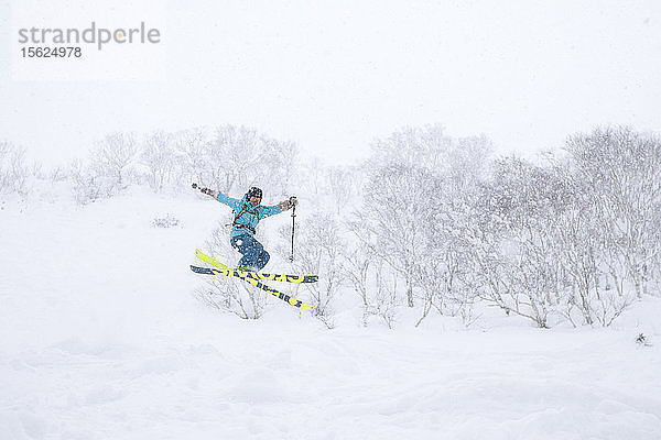 Eine Skilangläuferin springt auf halber Höhe des Vulkans Annupuri im Skigebiet Niseko United in die Luft. Der Schnee auf der japanischen Insel Hokkaido ist so tief und flauschig  dass er ein Paradies für Tiefschneefahrer ist und große Sprünge ermöglicht  da die Landung immer weich ist. Niseko United besteht aus vier Skigebieten auf dem Annupuri (1.308 m)  einem einzigen Berg. Der 100 km südlich von Sapporo gelegene Niseko Annupuri ist Teil des Quasi-Nationalparks Niseko-Shakotan-Otaru Kaigan und ist der östlichste Park der Niseko-Vulkangruppe. Hokkaido  die nördliche Insel Japans  liegt geografisch ideal in der Bahn der beständigen Wettersysteme  die die kalte Luft aus Sibirien über das Japanische Meer bringen. Dies führt dazu  dass viele der Skigebiete mit Pulverschnee überhäuft werden  der für seine unglaubliche Trockenheit bekannt ist. In einigen der Skigebiete Hokkaidos fallen durchschnittlich 14-18 Meter Schnee pro Jahr. Niseko ist die Pulverschneehauptstadt der Welt und als solche das beliebteste internationale Skigebiet in Japan. Es bietet ein unvergessliches Erlebnis für Skifahrer und Snowboarder aller Niveaus.