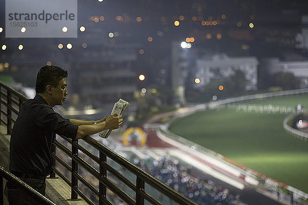 Foto eines Mannes  der auf einer Pferderennbahn Wetten liest  Hongkong  China