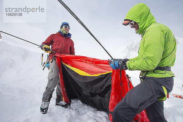 Zwei Bergsteiger bauen bei kaltem und stürmischem Wetter ein Zelt auf dem Denali auf