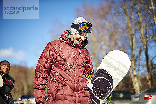 Ein männlicher Snowboarder geht mit seinem Brett und lacht