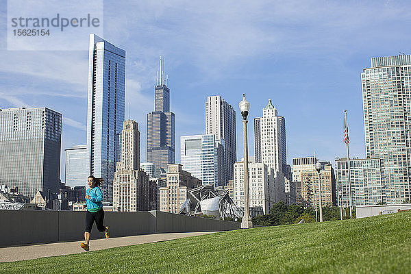 Eine erwachsene Frau läuft durch den Millenium Park mit der Skyline der Innenstadt von Chicago im Hintergrund. Chicago  Illinois.