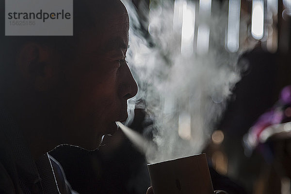 Ein Mann raucht in seinem Haus in Ban Sop Kha  Laos  eine Zigarette durch eine große Wasserpfeife aus Bambus. Der Mann erklärte  dass das Rauchen von Zigaretten auf diese Weise besser für seine Lunge sei.