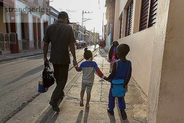 Vater  Sohn und Tochter gehen zusammen auf dem Bürgersteig und halten sich an den Händen  Santiago de Cuba  Kuba
