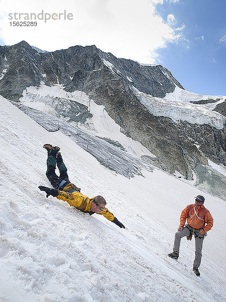 Bei einem Sicherheitstraining für Bergsteiger rutscht ein Schüler einen steilen Gletscherhang hinunter und versucht  sich abzusichern  während der Lehrer  ein Bergführer  Ratschläge gibt  Moiry-Gletscher  Wallis  Schweiz