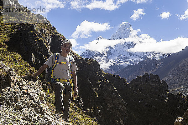 Sange Sherpa  ein nepalesischer Bergführer  steht für ein Foto entlang der Trekkingroute zum Everest-Basislager  in der Ferne ist die Ama Dablam zu sehen  die der Führer bereits bestiegen hat  Phortse  Solu Khumbu  Nepal