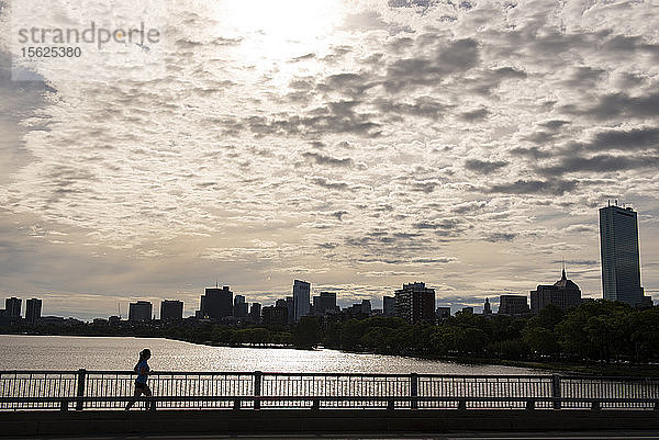 Silhouette einer Frau  die bei Sonnenuntergang auf einer Brücke am Charles River läuft  Boston  Massachusetts  USA