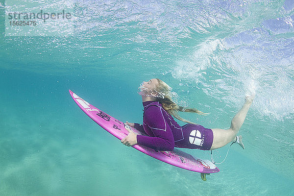 Unterwasserfoto eines blonden Surfermädchens mit einem kurzen Neoprenanzug  das unter einer Welle hindurchtaucht