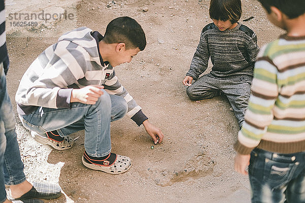 Foto eines Jungen aus dem Westen  der mit marokkanischen Kindern auf der Straße Murmeln spielt  Marrakesch  Marokko