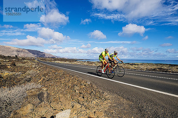 Zwei Rennradfahrer fahren nebeneinander auf einer Straße in Küstennähe  Lanzarote  Kanarische Inseln  Spanien