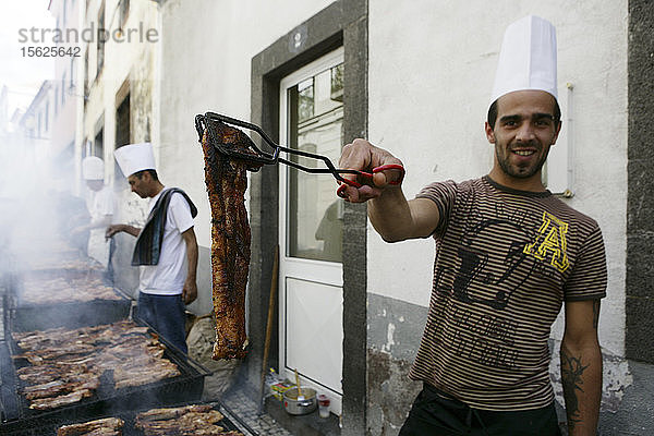 Ein junger Mann bietet Fleisch vom Grill an  der auf der Straße aufgestellt ist  Funchal  Madeira  Portugal