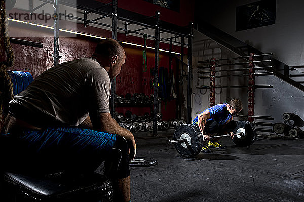 Ein sportlicher Mann trainiert mit schweren Gewichten an einer Langhantel  während sein Partner in San Diego  Kalifornien  zusieht.