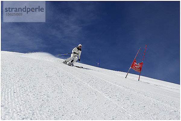 Ältere Skifahrerin auf einer Skipiste an einem sonnigen Tag mit blauen Skiern und weißem Ski-Outfit