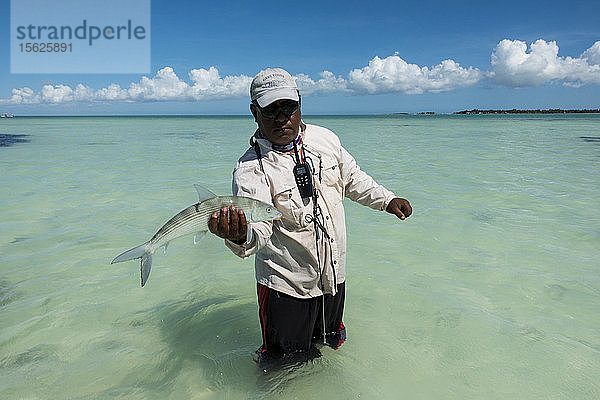 Mann steht im Küstenwasser und posiert mit einem gefangenen Bonefish  Kiribati
