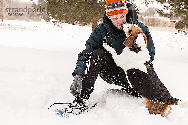 Mann beim Schneeschuhwandern mit seinem Beagle