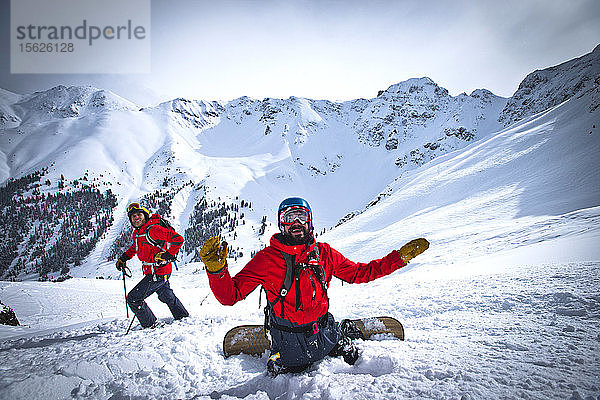 Ein Skifahrer und ein Snowboarder halten an  um ihren Freunden bei der Abfahrt auf dem Silverton Mountain in Colorado zuzusehen.