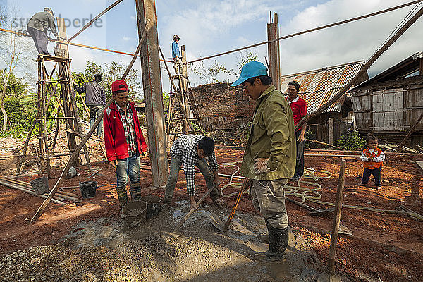 Männer bauen ein neues Haus mit modernen Materialien in Boun Neua  Provinz Phongsaly  Laos  während ein kleines Mädchen zusieht.