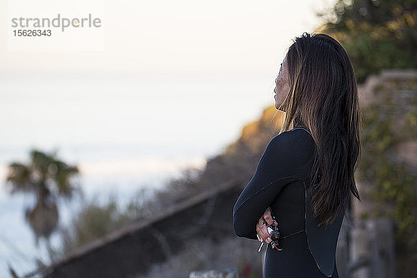 Eine Surferin beobachtet die Wellen vor einer Surfsession bei Sonnenaufgang in San Diego  Kalifornien