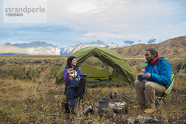 Ehepaar isst beim Zelten vor einem Zelt mit den Bergen der Teton Range im Hintergrund  Jackson  Wyoming  USA