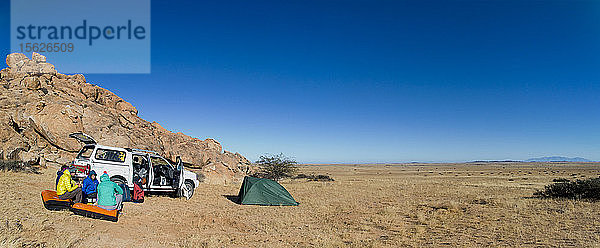 Gruppe von Menschen sitzt neben einem Auto in der Wüste  Spitzkoppe  Erongo-Region  Namibia