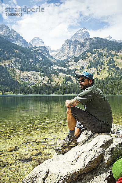 Ein Rucksacktourist sitzt auf einem Felsen an einem See in den Grand Teton Mountains in Jackson Hole  Wyoming