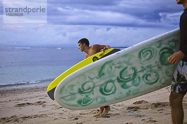 Zwei Surfer  die ihr Surfbrett am Strand tragen