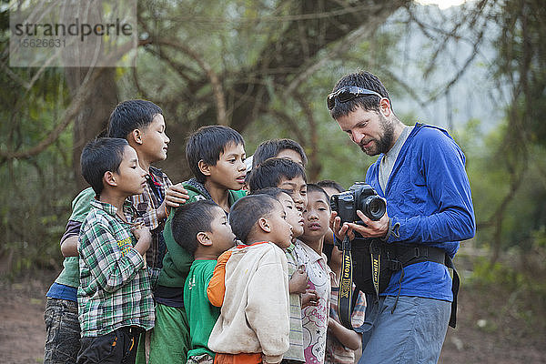 Robert Hahn zeigt einer Gruppe neugieriger Jungen am Strand von Muang Hat Hin  Laos  Bilder von der Rückseite seiner Digitalkamera.