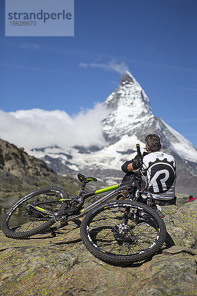 Ein Mountainbiker ruht sich aus und genießt die Aussicht auf das Matterhorn  einen berühmten Berg oberhalb von Zermatt in den Schweizer Alpen.