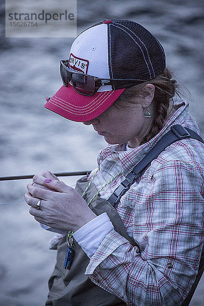 Eine Frau wechselt beim Fliegenfischen in der Abenddämmerung in Montana die Fliegen.