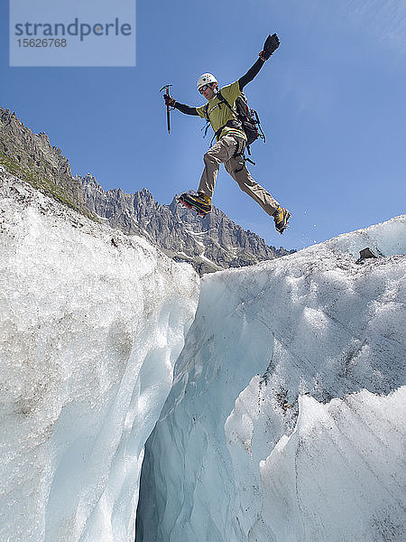 Ein Bergsteiger springt über eine Gletscherspalte am Mer de Glace  einem berühmten Gletscher im Mont-Blanc-Gebirge.