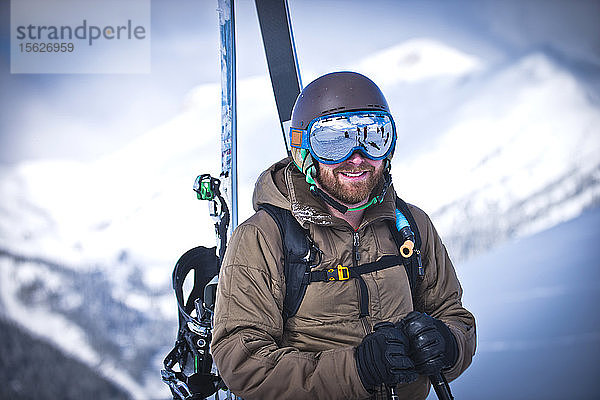 Ein Skifahrer lächelt an einem sonnigen Tag  als er auf dem Gipfel des Silverton Mountain in Colorado wandert.