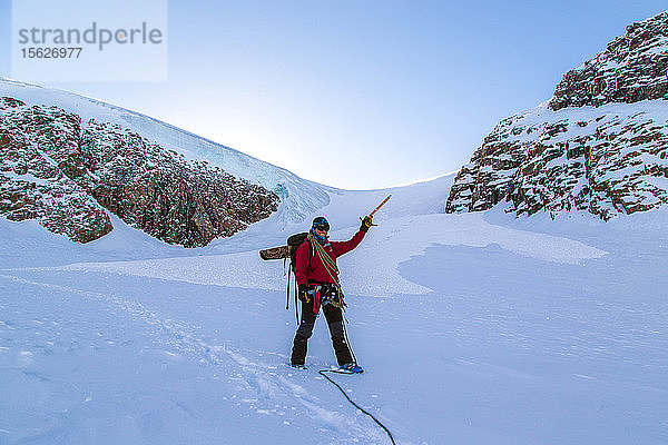 Zac Poulton zeigt mit seinem Eispickel auf sein Bergsteigerteam in den Stauninger Alpen von Grönland