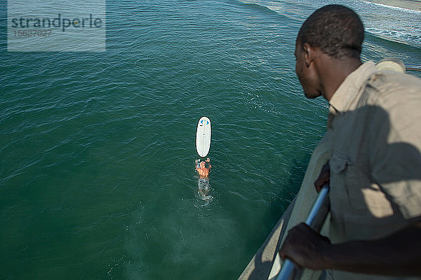 Mann auf dem Pier  der einem Surfer beim Paddeln auf dem Surfbrett nahe der Promenade an der Golden Mile zusieht  Durban  Südafrika